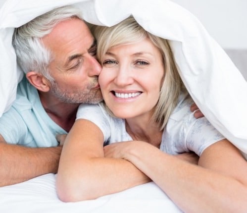 Older man kissing wife on the cheek while she smiles and looks at the camera