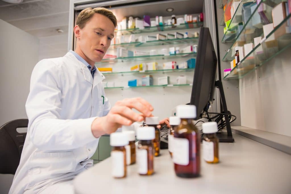 Pharmacist typing in information into computer while looking at medication bottles